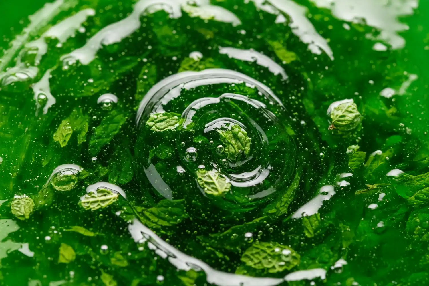 Feuilles de menthe verte immergées dans un liquide clair, bulles visibles, symbolisant la fraîcheur stimulante de la menthe.