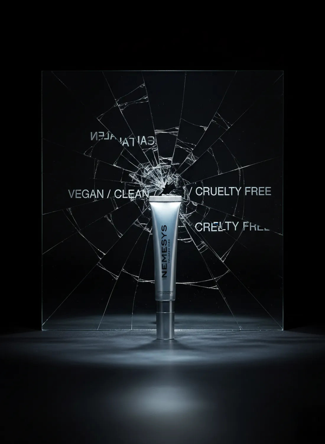Tube de gloss repulpant NEMESYS chrome, posé devant un miroir fissuré portant les mentions vegan clean cruelty free, visuel radical contre le greenwashing.