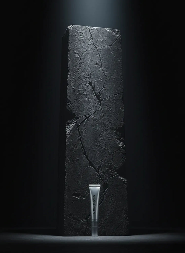 Gloss repulpant NEMESYS posé devant un bloc de pierre noire craquelée, éclairage dramatique qui souligne la puissance et la sobriété de la formule.