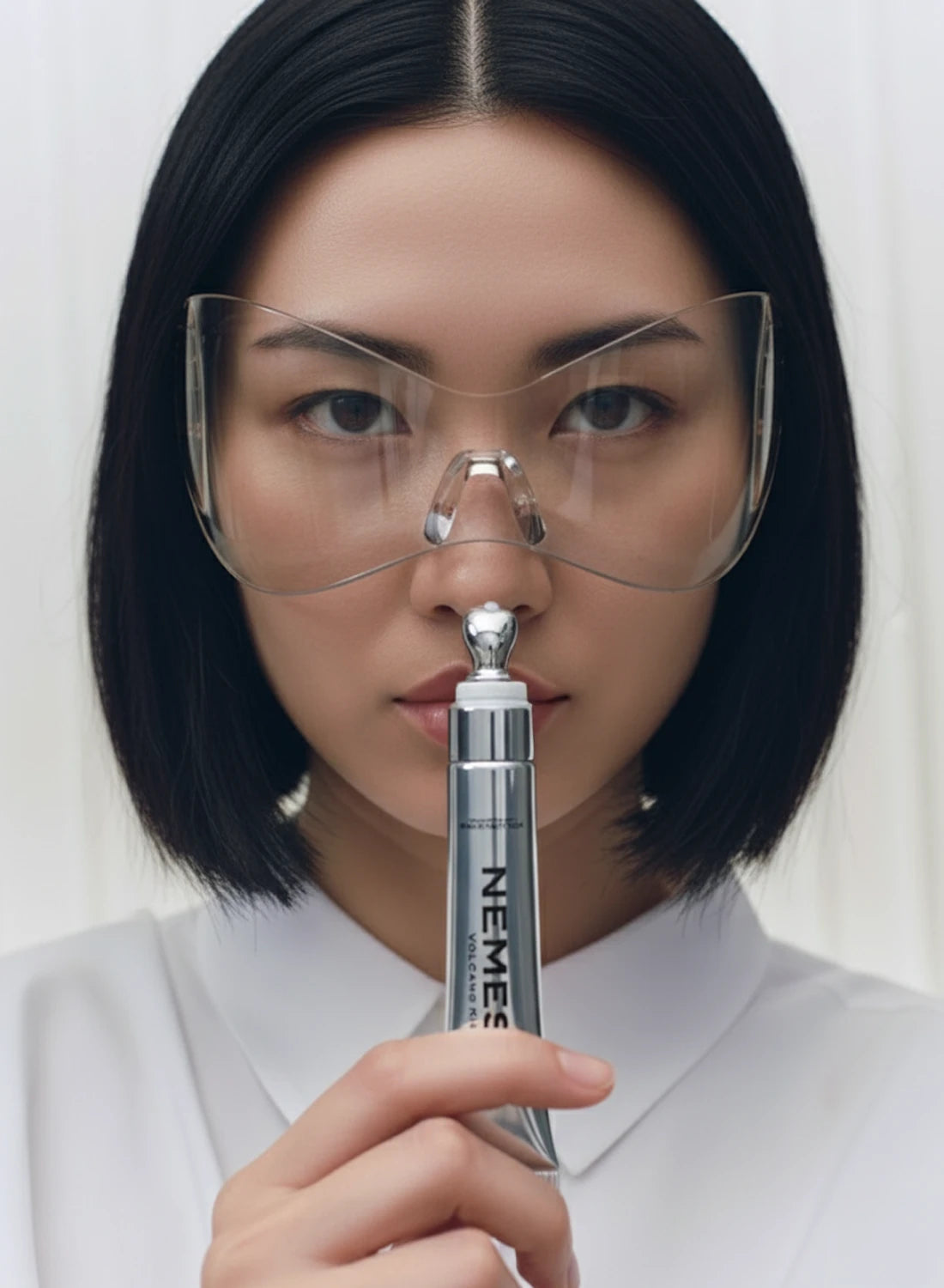 Femme en blouse blanche et lunettes de laboratoire tenant un gloss NEMESYS argenté, ambiance scientifique premium.