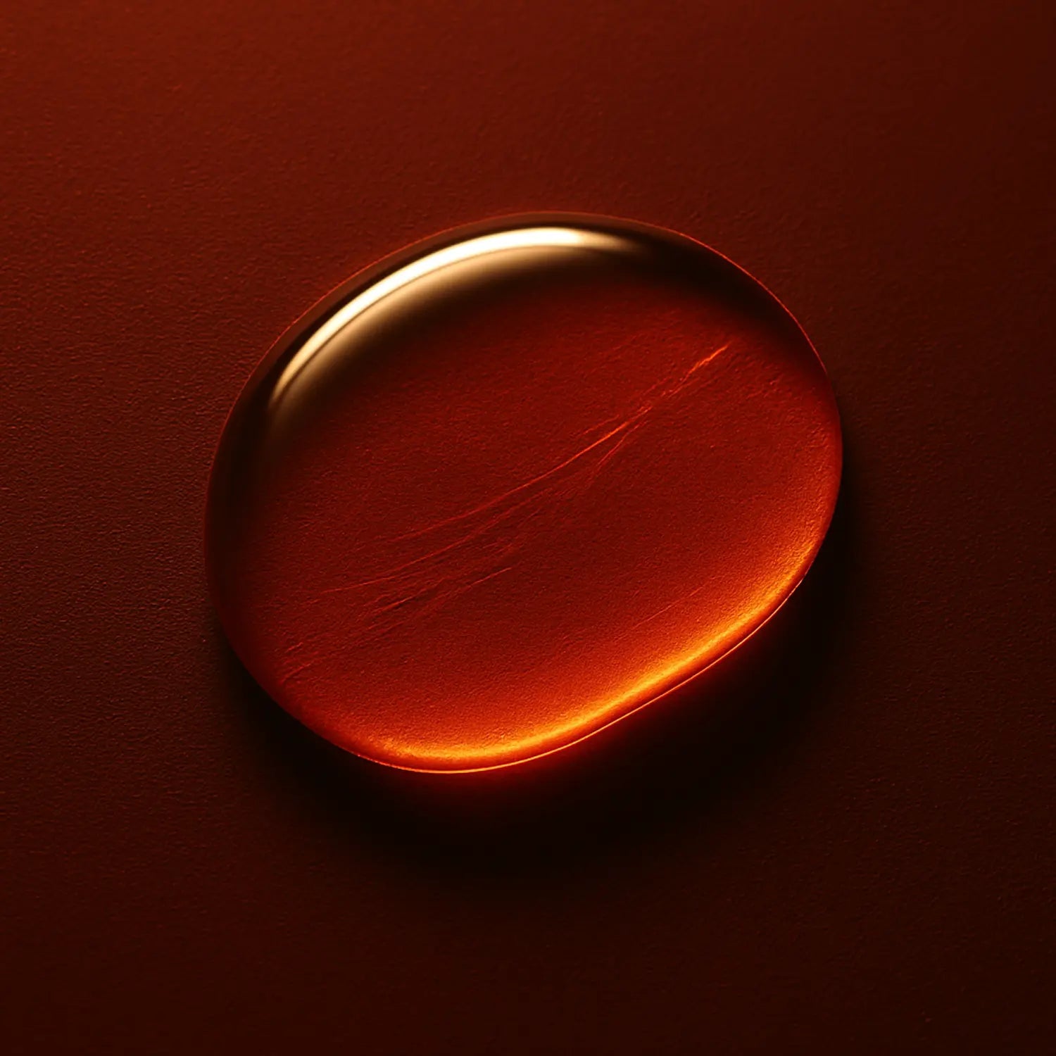 Goutte aplatie de Vanillyl Butyl Ether sur fond rouge volcanique mat, éclairée en biseau par une lumière chaude contrôlée — texture lisse et dense, forme organique étirée, évoquant une stimulation thermique progressive et ciblée — sensation de frisson maîtrisé, sans inflammation.